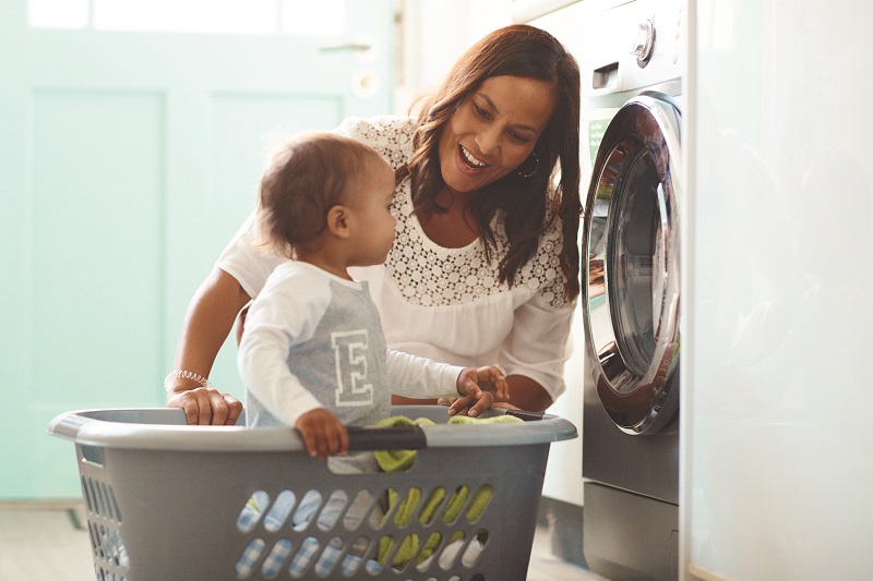 Woman smiles at toddler sitting in washing basket