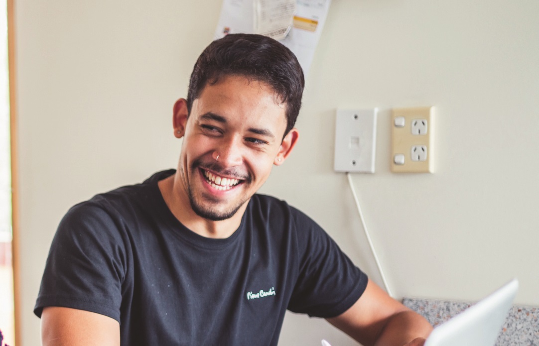 Man smiles at another person while using laptop