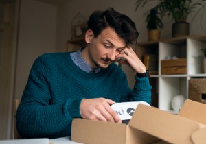 A man with an annoyed look on his face, looking down at a product he bought which could be faulty 