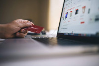 Hand holds a payment card at a laptop
