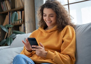 A female sitting on a couch smiling down at her phone.